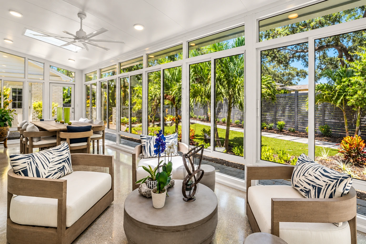 Custom sunroom with floor-to-ceiling white-framed windows, modern seating and views of a tropical garden.