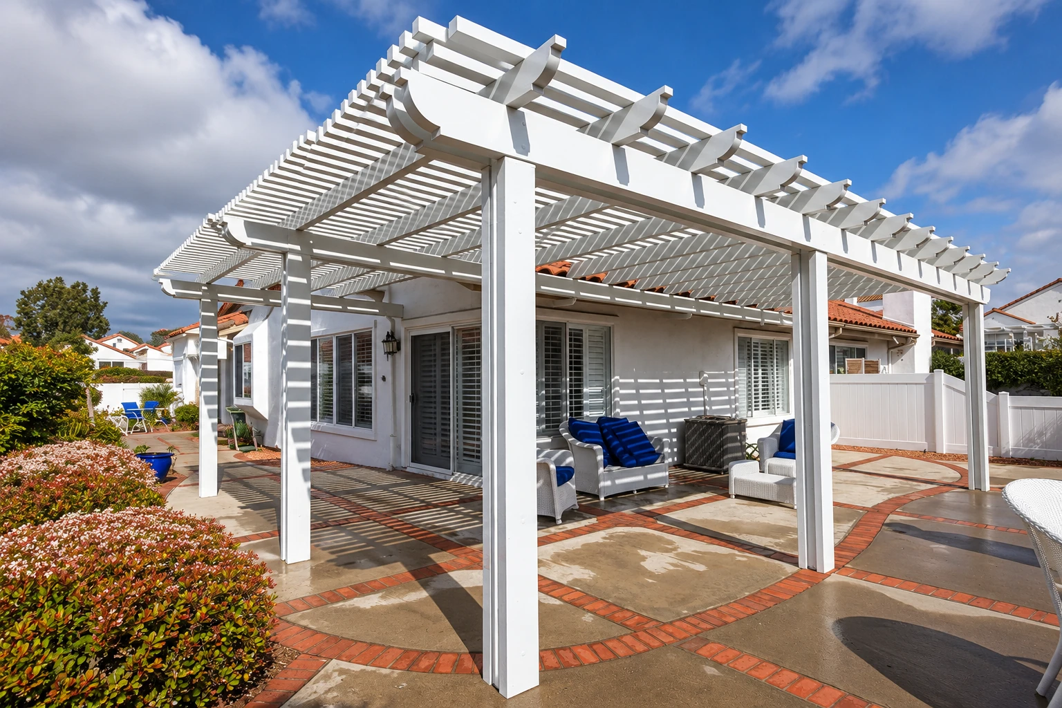 White pergola patio cover shading an outdoor seating area beside a house.