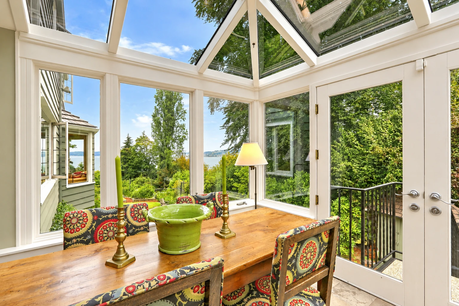 Sunroom addition with glass walls and a skylight roof, furnished with a long dining table beside leafy views.
