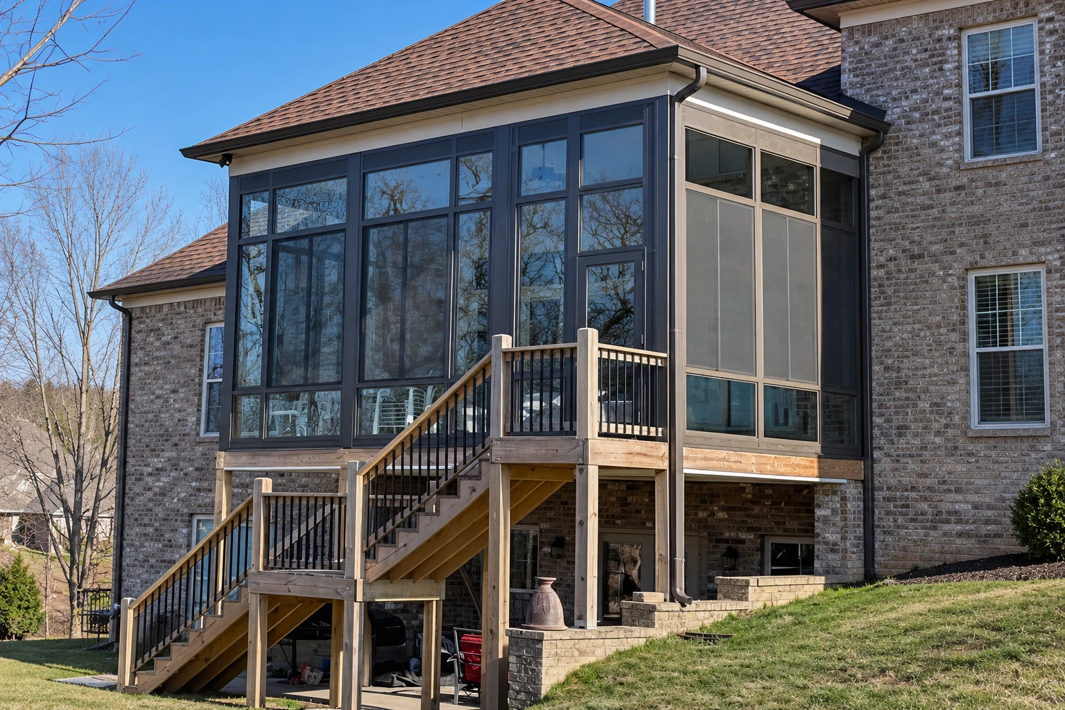 Two-story brick home with an enclosed sunroom addition featuring dark-framed windows and a raised wooden staircase and deck.
